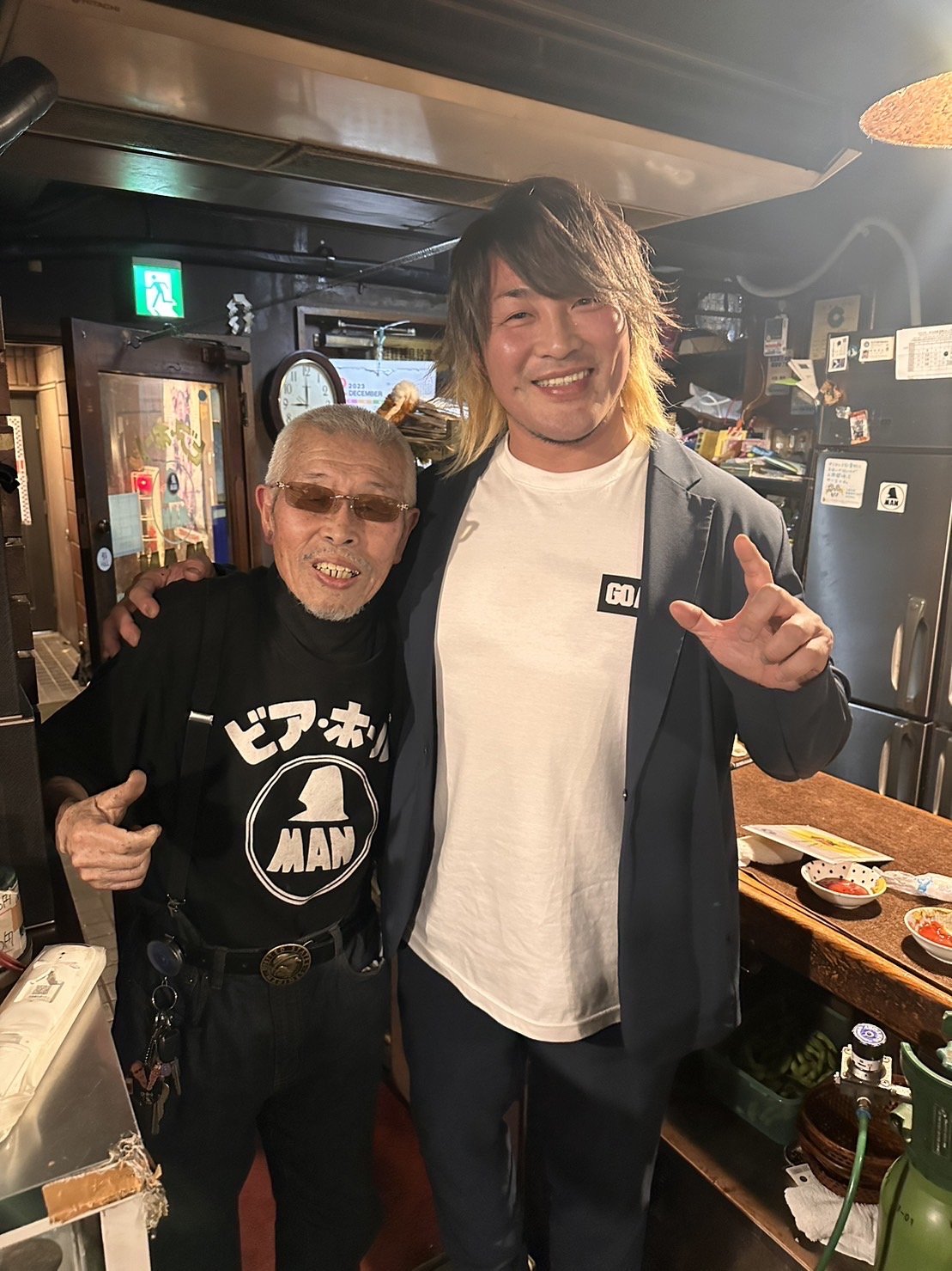 店内でレスラーと並んでポーズを取る村田マスター