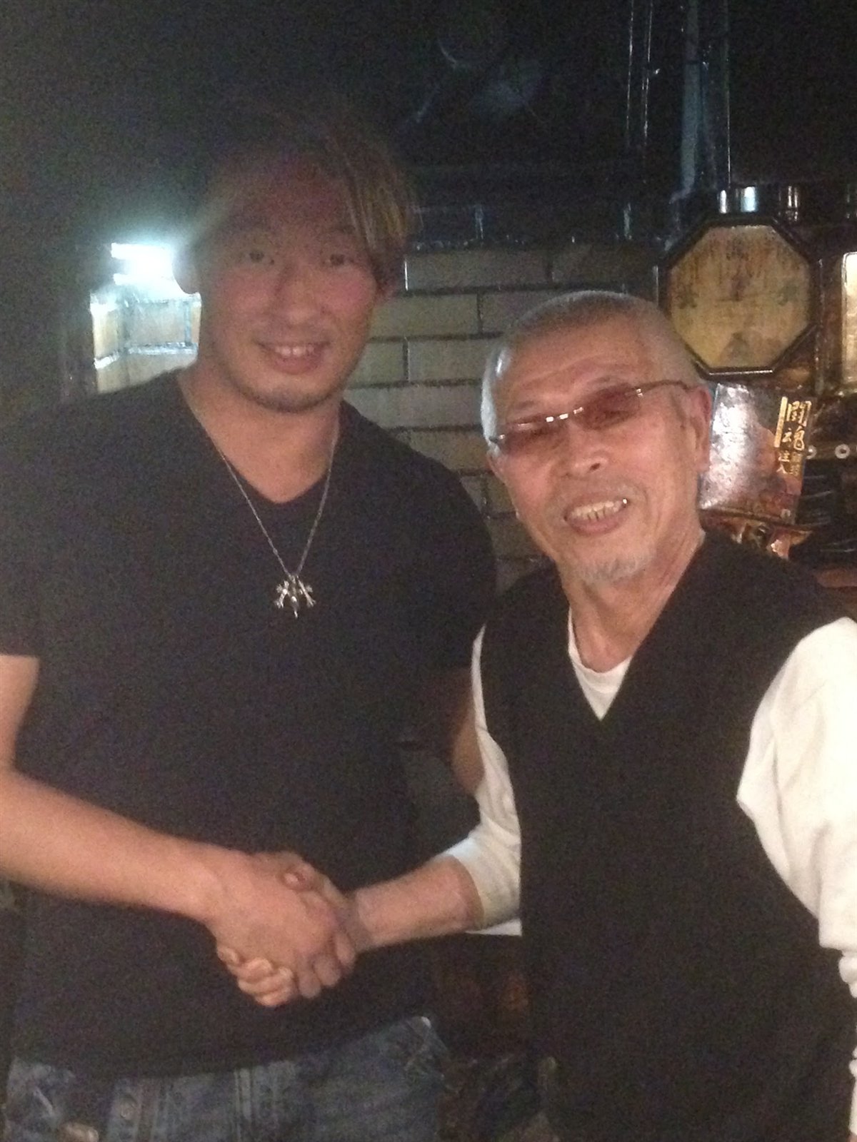 店内でレスラーと笑顔で握手する村田マスター